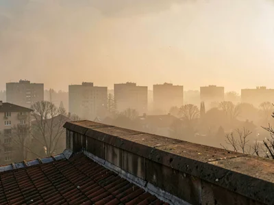 A tar rooftop's parapet edge meets a sweeping painterly view of distant smog-sof