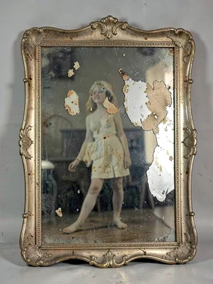 An antique mercury mirror with deteriorating silver, figure visible through pati
