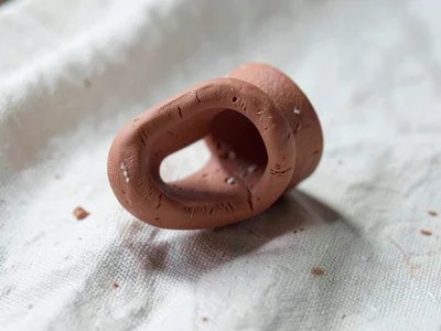 Chiseled terracotta mug handle as a fragment, thumb-pressed snap, on plain pale 
