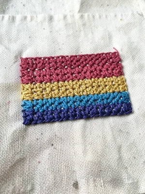 Hand-stitched pride flag on cotton, each stripe a different thread texture