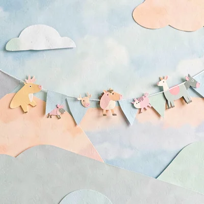 Cut-paper banner of a parade of paper animals across a horizon, peach and sage