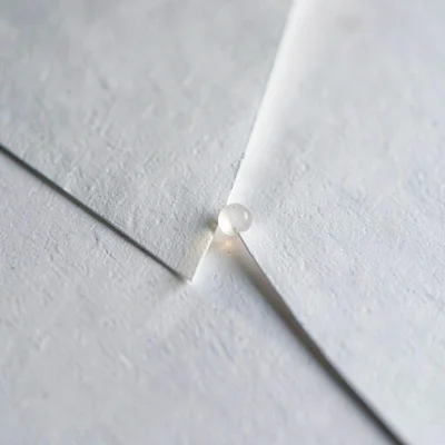 Two paper tongues meeting at a sharp diagonal seam, single bead of light running
