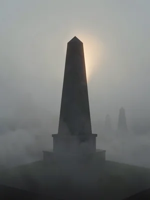 Stone obelisk monument emerging from a low fog bank with a faint warm rim of lig