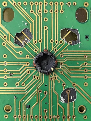 A damaged PCB with a burnt component leaving a dark scorch mark on the green sol