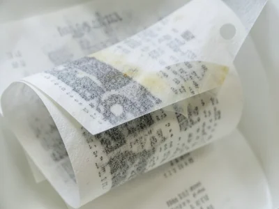 Stack of curled thermal receipts on lightbox, overlapping translucent papers cre