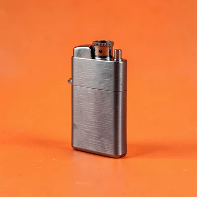 small refillable lighter in brushed gunmetal at three-quarter angle on a saturat