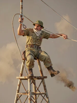 A signal-tower-climber clips a carabiner to an unseen line, mouth-cloth pulled u