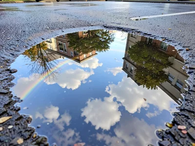 Spring sky and clouds captured in parking lot puddle, oil rainbow at edge