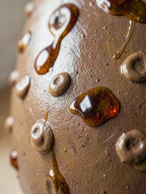 Hand-pressed thumb dents alternating up the wall of an earthenware piece, glaze