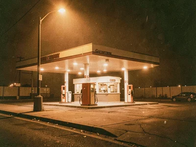 Gas station at night, sodium vapor turning everything amber, lonely pumps