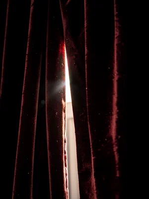 Velvet curtain partially drawn, light streaming through gap, theatrical reveal