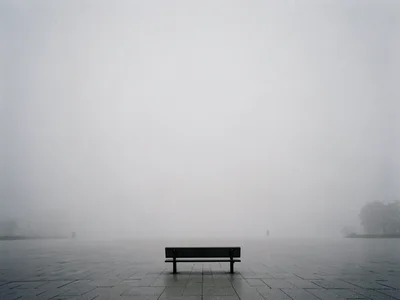 Single bench at frame edge surrounded by vast empty plaza in fog