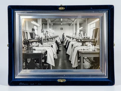 A row of industrial sewing machines in a garment factory with fabric flowing thr