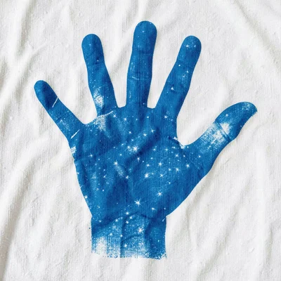A hand splayed wide, fingers spread, pressed onto cotton — strong blue silhouett
