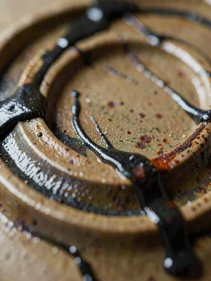 Drips of tenmoku running over wheel ridges, dark glaze sliding into the troughs 