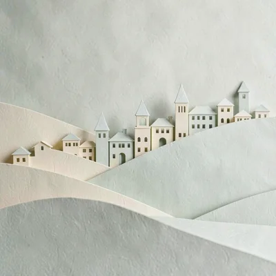 Papercraft composition of a layered paper-cut town silhouette across rolling pap
