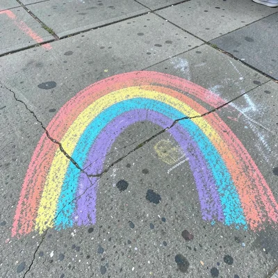 A chalk rainbow arcing across a wide sidewalk, each color band thick and vivid, 