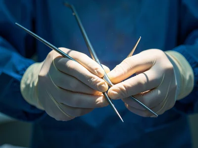 A surgeon's hands with surgical instruments, lit to make the gloves glow and the