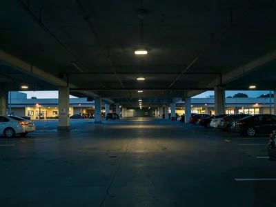 Shopping mall parking structure at dusk, cars sparse, lights buzzing on