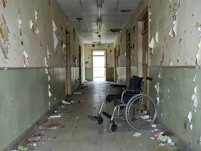 Decommissioned asylum hallway, wheelchair abandoned mid-frame, wallpaper peeling