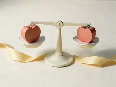 A papercraft scale balanced exactly level with one curved paper apple in each pa