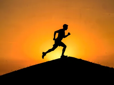 Runner cresting hill at sunrise, complete silhouette against nuclear orange sky
