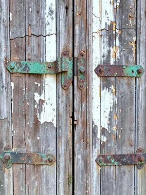 Weathered wooden door with cracked paint, iron hinges covered in verdigris