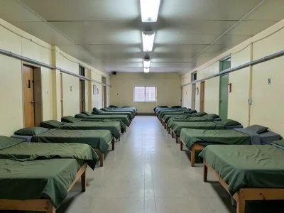 Military barracks, rows of identical beds from center aisle, overhead fluorescen