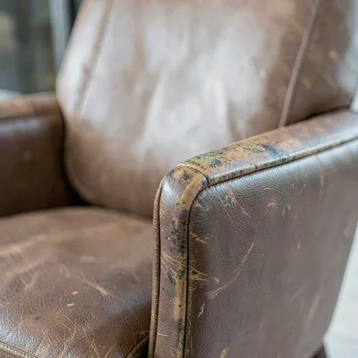 Tight crop of worn leather chair arm with patina, hard side light