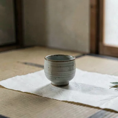 A solitary small ceramic sake cup with unglazed rim resting on hand-deckled rice