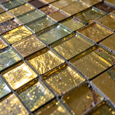 Close-up of gilded glass tesserae at a raking angle — the gold layer visible ben