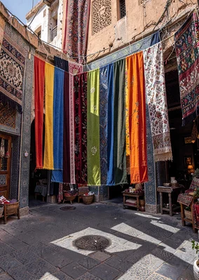 Geometric shadow play in Marrakech medina, textile souk with hanging fabrics cre