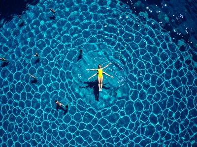 A person in a yellow swimsuit floating face-up in a deep blue ocean, their body 