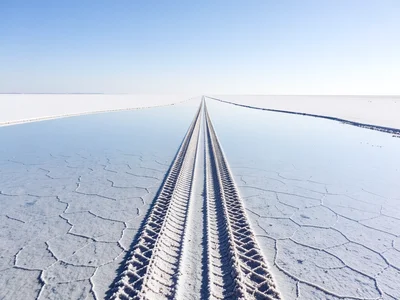 Tire tracks through flooded salt flat — two parallel lines cutting through the r