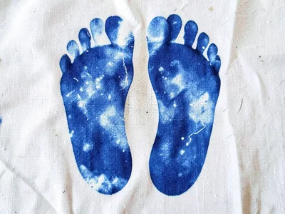 A pair of bare feet pressed onto cyanotype linen — foot outlines in Prussian blu
