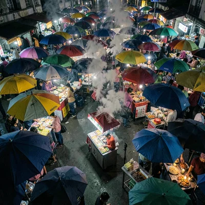 Night market from above, maze of umbrellas and steam, focus on single vendor