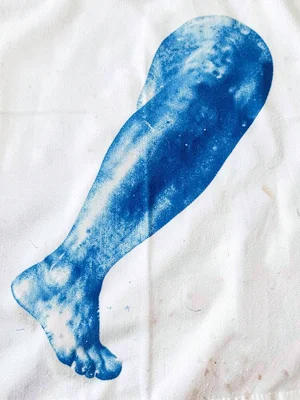 A knee and lower leg pressed onto cyanotype cotton — curved form in blue on whit