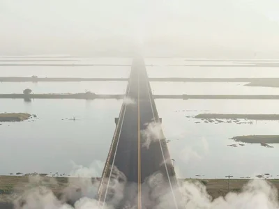 Long causeway lifting through tidal flats, water on either side mirror-pale, the