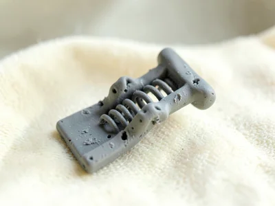 Pegged putty-grey laundry pin with a slumped spring and fingernail dents along i