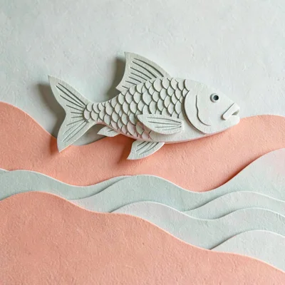 Papercraft hero of a layered paper-cut fish above paper-cut waves, soft sage and