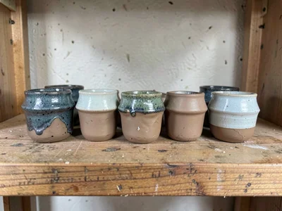 A row of small pinch pots drying on a wooden shelf, raw clay surface