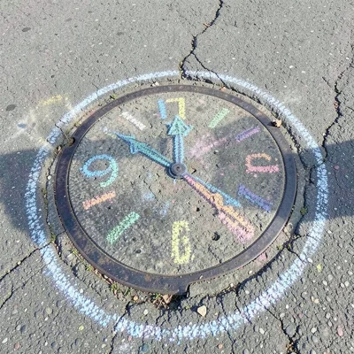 A chalk clock face drawn around a manhole cover, the cover becoming the clock ce
