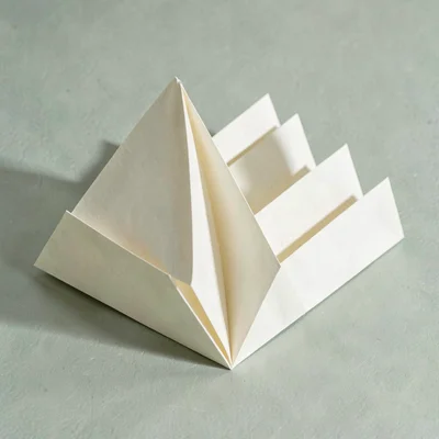Single sheet of cream paper folded into a stepped fan, casting a soft layered sh