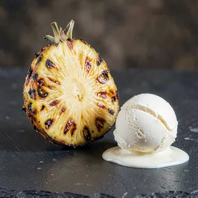 Single charred half-pineapple on dark slate, deep amber caramelization on the cu