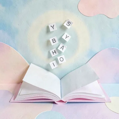 Cut-paper still of a paper open book with paper letters drifting up, calm halo