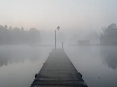 A pier extending into a foggy lake, the planks disappearing after 30 feet, a sin