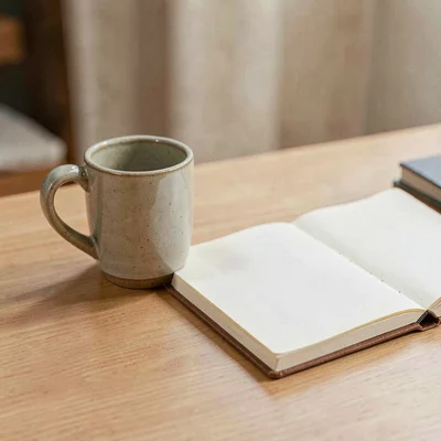 Minimal still of a single ceramic mug beside an open blank journal