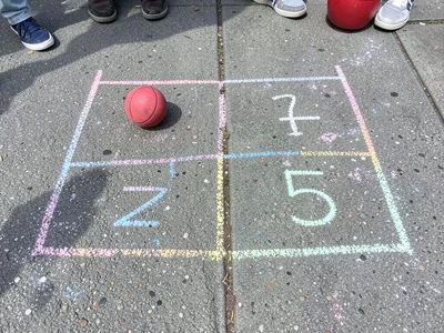 A game of four-square drawn in chalk, the squares numbered, a bouncy ball in one