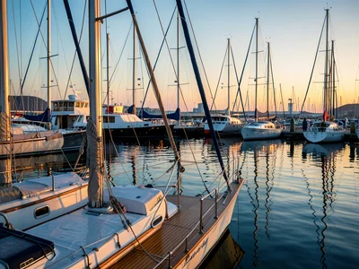 A sailboat marina at golden hour: masts creating vertical lines, halyards clinki