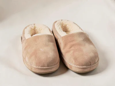 One pair of soft suede slippers sits paired showing fleece-lined interiors and r